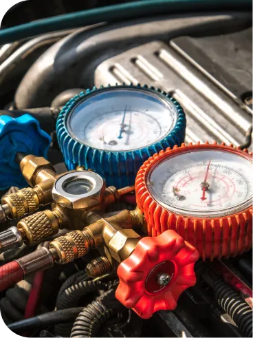 A close-up of automotive air conditioning manifold gauges with blue and red dials, placed on a car engine for diagnostic or maintenance work.