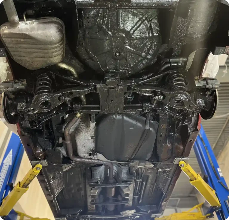 A car is lifted on a hydraulic lift, showing the undercarriage, including suspension components, exhaust system, and chassis, all appearing clean and recently serviced.
