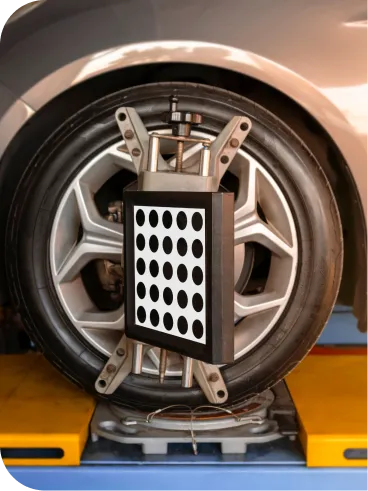 A car wheel with a device attached, featuring a panel of black and white dots, is set up for a wheel alignment check in an auto repair shop.