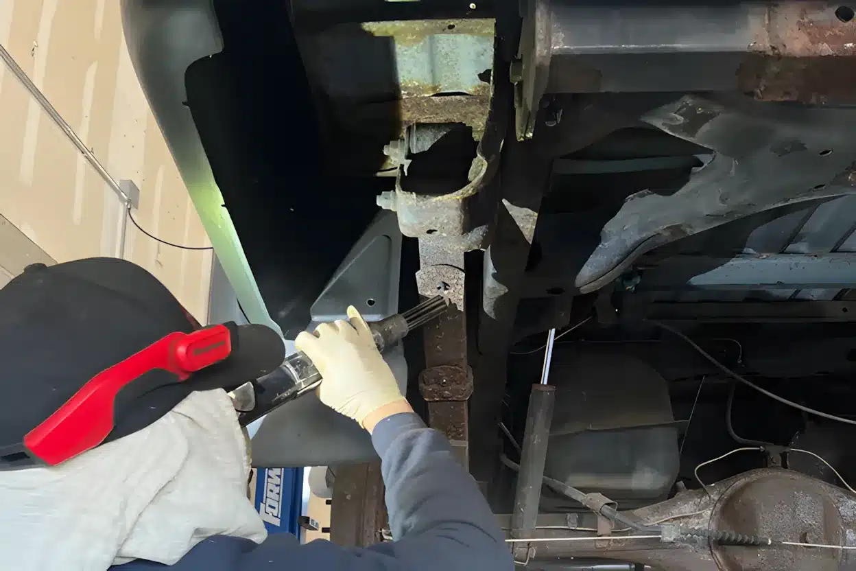Auto technician wearing gloves and head protection working under a vehicle.