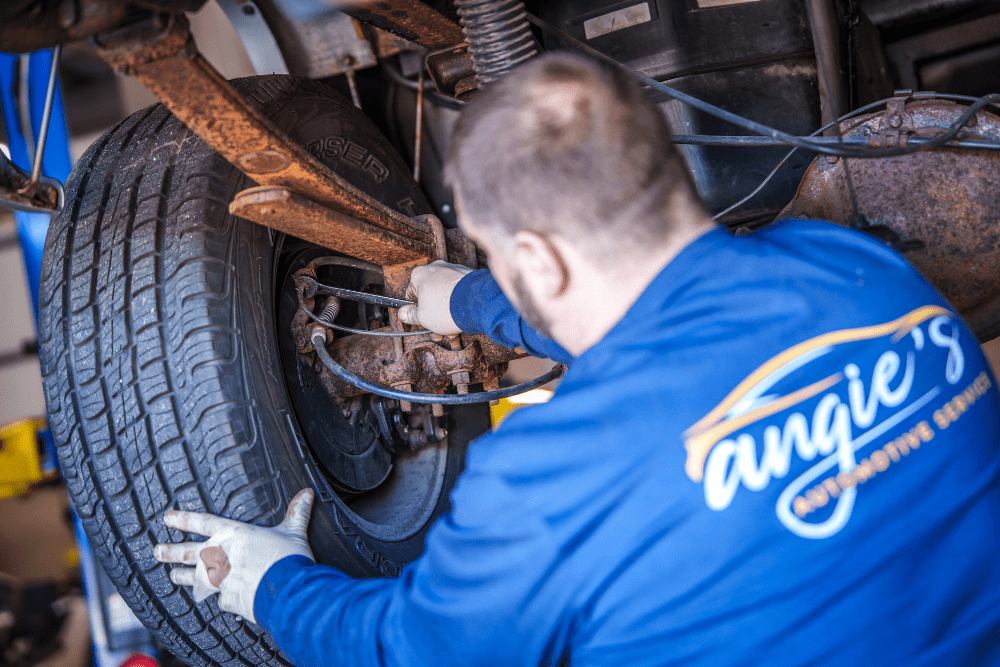 Car maintenance, auto repair in Newbury, MA by Angie’s Service Inc. Image of a technician working on a vehicle’s suspension and wheel assembly, showcasing professional care to ensure safe handling and reliable performance.