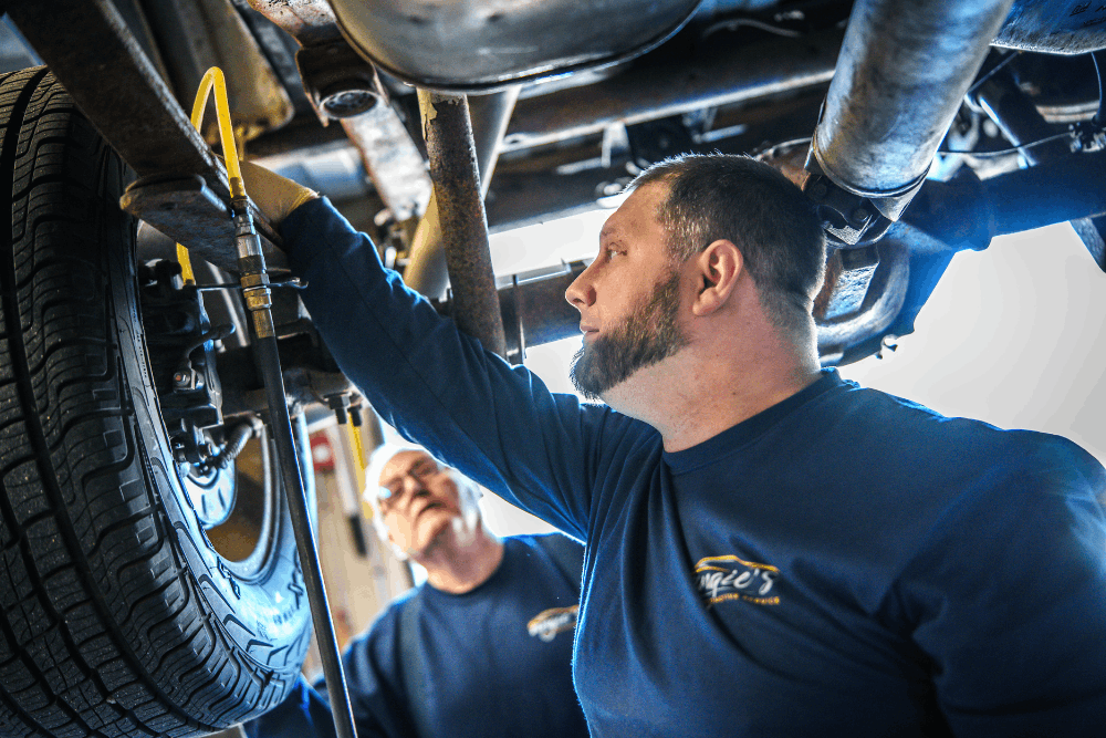 Vehicle inspection, auto repair in Newbury, MA at Angie's Service Inc. Image of technicians inspecting a vehicle’s wheel and undercarriage during service.